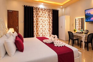 Quarto de hotel com cama, escrivaninha, cadeira, guarda-roupa e televisão.