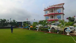 A multi-story building with a balcony, surrounded by a well-maintained lawn and parked cars.