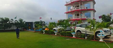 A multi-story building with a balcony, surrounded by a well-maintained lawn and parked cars.