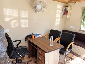 A small office space with a desk, two chairs, a fan, and a shelf with decorative items. - THE VRINDAVAN RESORT & BANQUET BY MTJ HOSPITALITY SERVICES LUCKNOW (Bakshi Ka Talab)