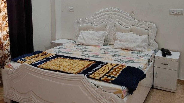 A bedroom with a white bed, a nightstand, a wall-mounted air conditioner, and a window with curtains.