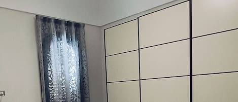 A bedroom with a bed, a chair, a wardrobe, and a window with curtains.