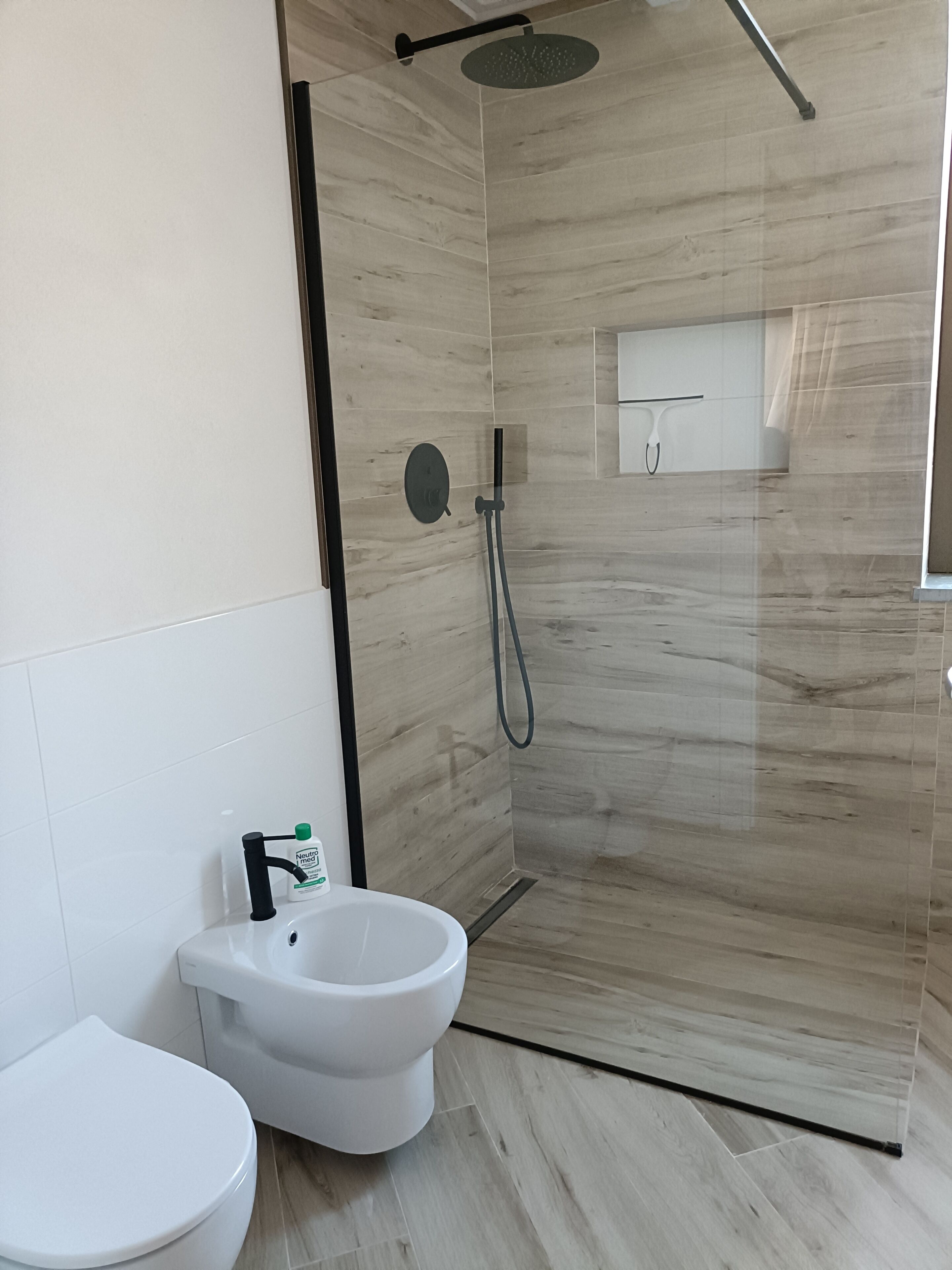 A modern bathroom with a glass-enclosed shower, a white toilet, and a bidet.