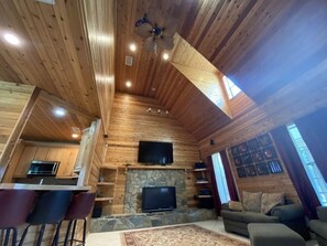 Ein Ferienhaus-Interieur mit Kamin aus Stein, einem darüber angebrachten Fernseher, einer Essecke mit Barhocker und einem Sofa im Wohnzimmer.