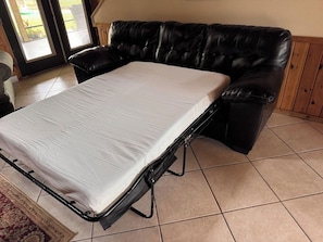 A room with a black leather sofa, a white mattress on a metal frame, and a tiled floor. - 4BR Salt Springs Retreat w/ Private Hot Tub (Salt Springs)