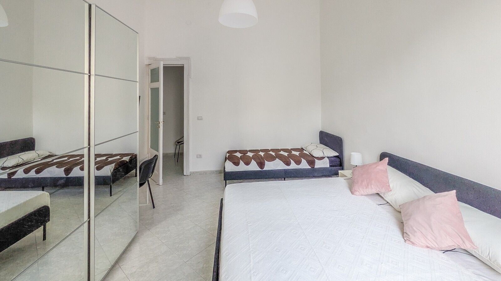 Een slaapkamer met twee bedden, een spiegel en een stoel.