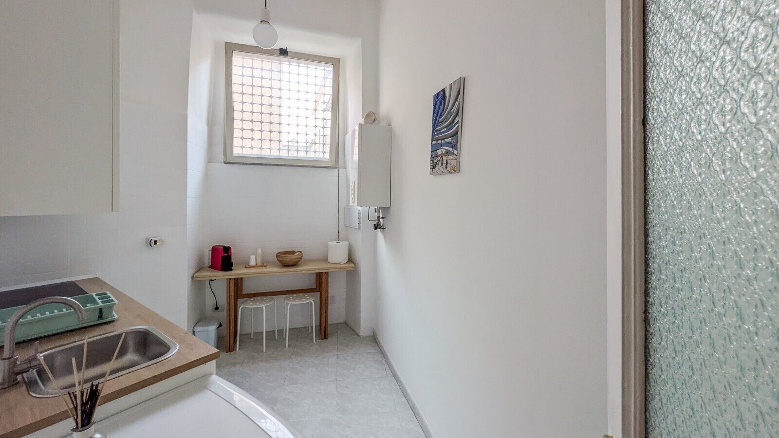 Eine kleine Küche mit Spüle, Tisch, Hocker und einem Fenster.