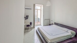 Un dormitorio con cama, escritorio, silla, radiador y ventana.