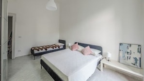 A bedroom with a large bed, a smaller bed, a bedside table, a lamp, and a painting on the wall. - Residenza Edoardo (Napoli)