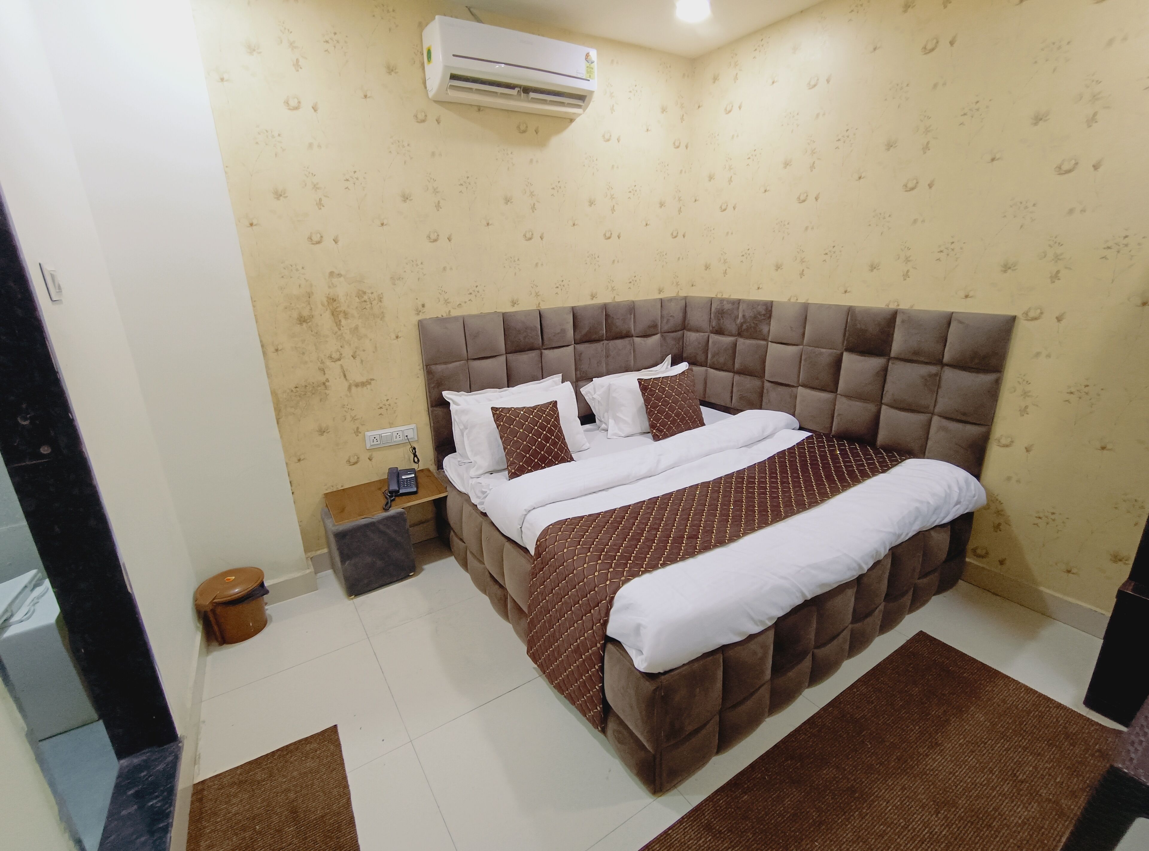 A hotel room with a large bed, a bedside table with a phone, and an air conditioning unit on the wall.