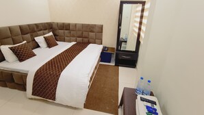 Habitación de hotel con una cama grande, una mesita de noche con espejo y un pequeño escritorio con teléfono y controles remotos.