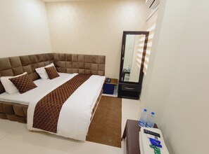 Habitación de hotel con una cama grande, una mesita de noche con espejo y un pequeño escritorio con teléfono y controles remotos.