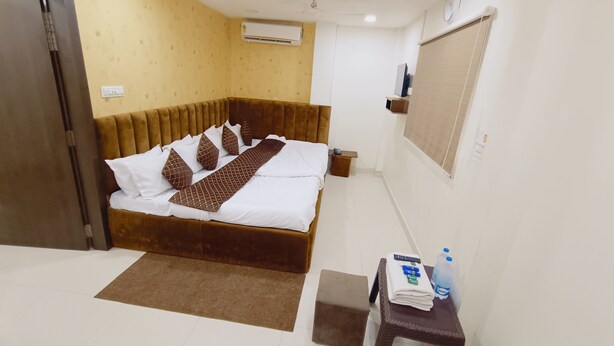 Habitación de hotel con cama, mesita de noche con una botella de agua, control remoto y una pequeña alfombra.