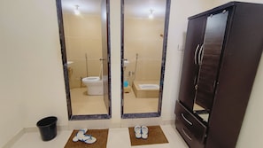 Un baño con inodoro, bidé y ducha. Hay un armario y un balde en el suelo.