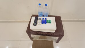 Una silla de mimbre con una toalla blanca, un control remoto, un teléfono móvil, dos botellas de agua y dos botellas verdes sobre un suelo de baldosas.