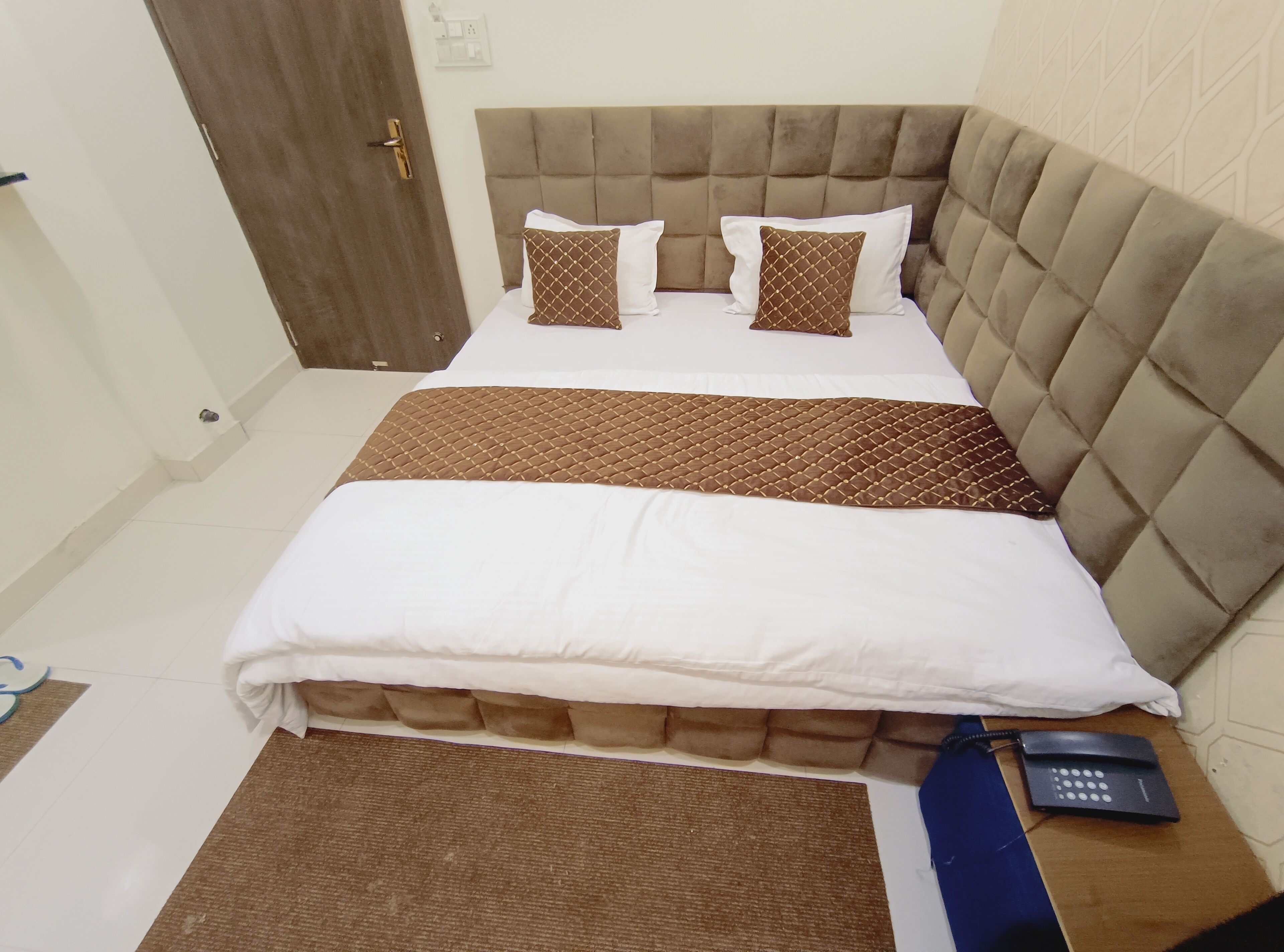 A neatly made bed with a tufted headboard, two pillows, and a brown bedspread.