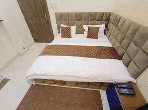 Una cama bien hecha con tablero tapizado, dos almohadas y una colcha marrón.