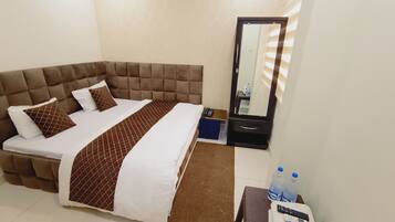 A hotel room with a large bed, a bedside table with a mirror, and a small table with a remote control and water bottles.