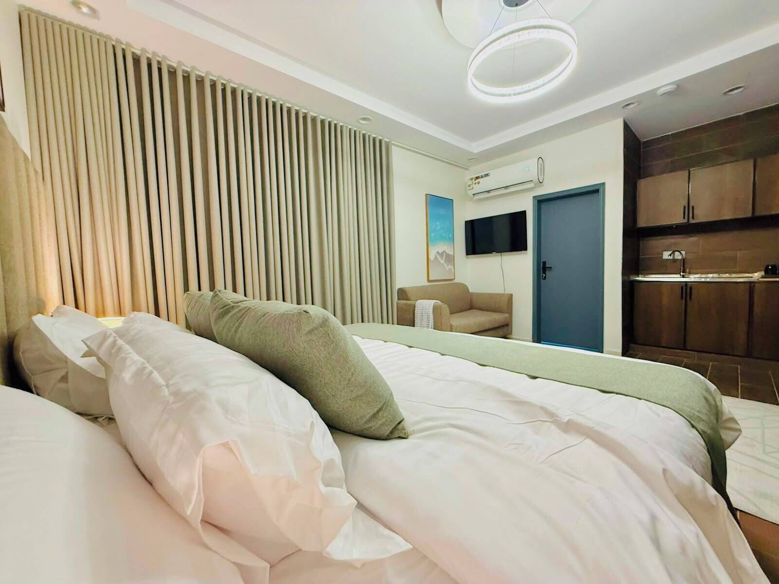 Habitación de hotel con cama, sofá, televisor, aire acondicionado y kitchenette.