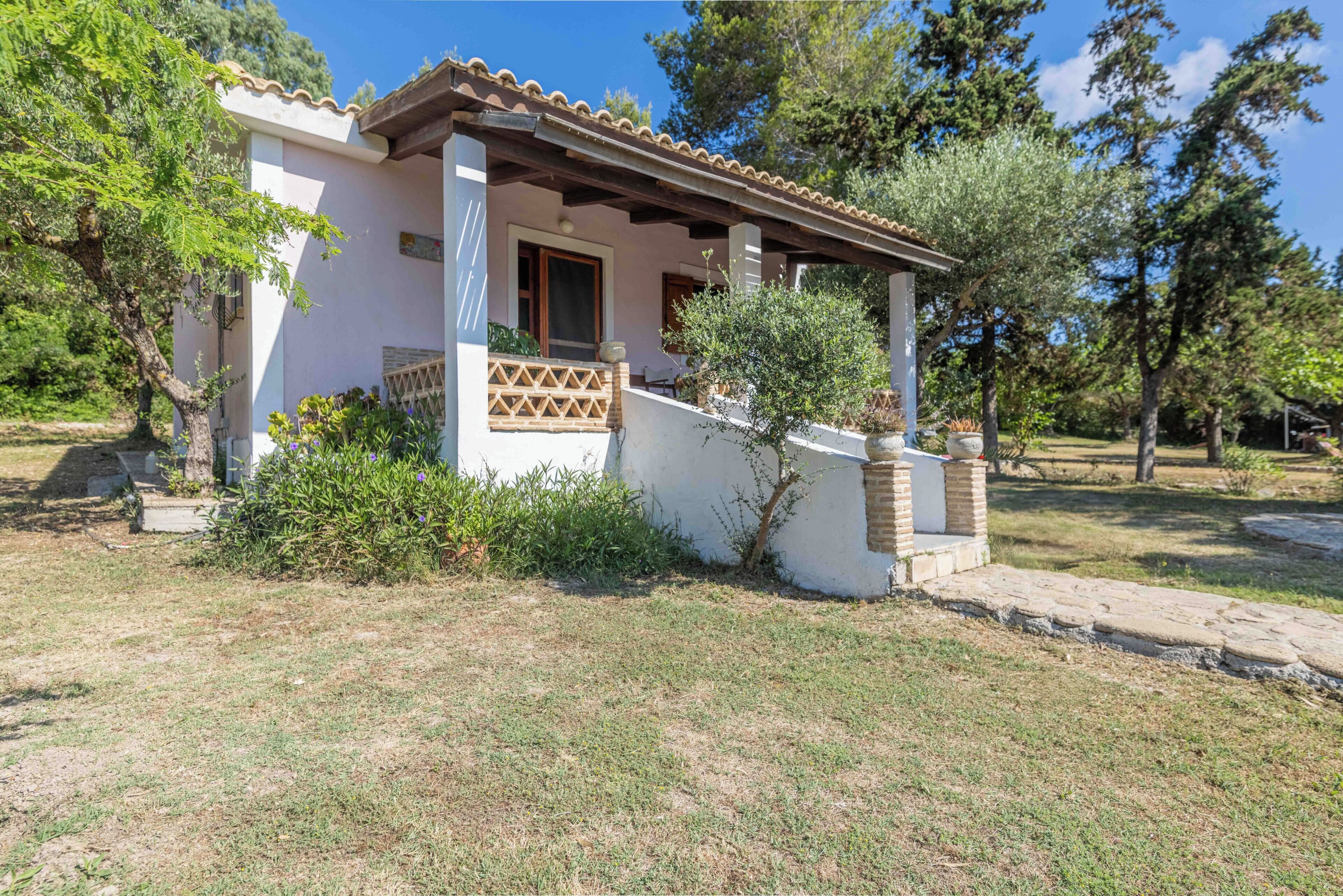 A single-story house with a tiled roof, a covered porch, and a small garden area.