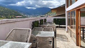 Una terraza con mobiliario de mimbre y vistas a una ciudad y montañas.