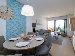 Ein modernes Wohnzimmer mit Essbereich, einer großen Uhr an der Wand und Blick ins Freie durch eine Schiebetür.