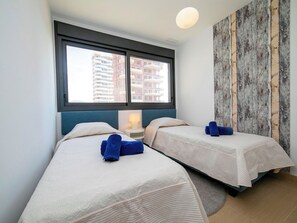 Ein Hotelzimmer mit zwei Betten, einem großen Fenster, einer Wand mit rustikaler Holzvertäfelung und einem kleinen Nachttisch mit Lampe.