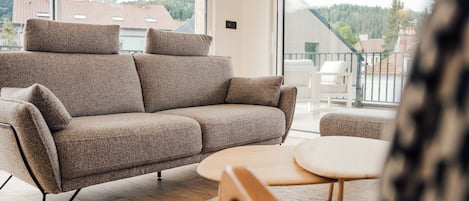 Una sala de estar moderna con un sofá, una mesita redonda y vistas al exterior a través de amplios ventanales.