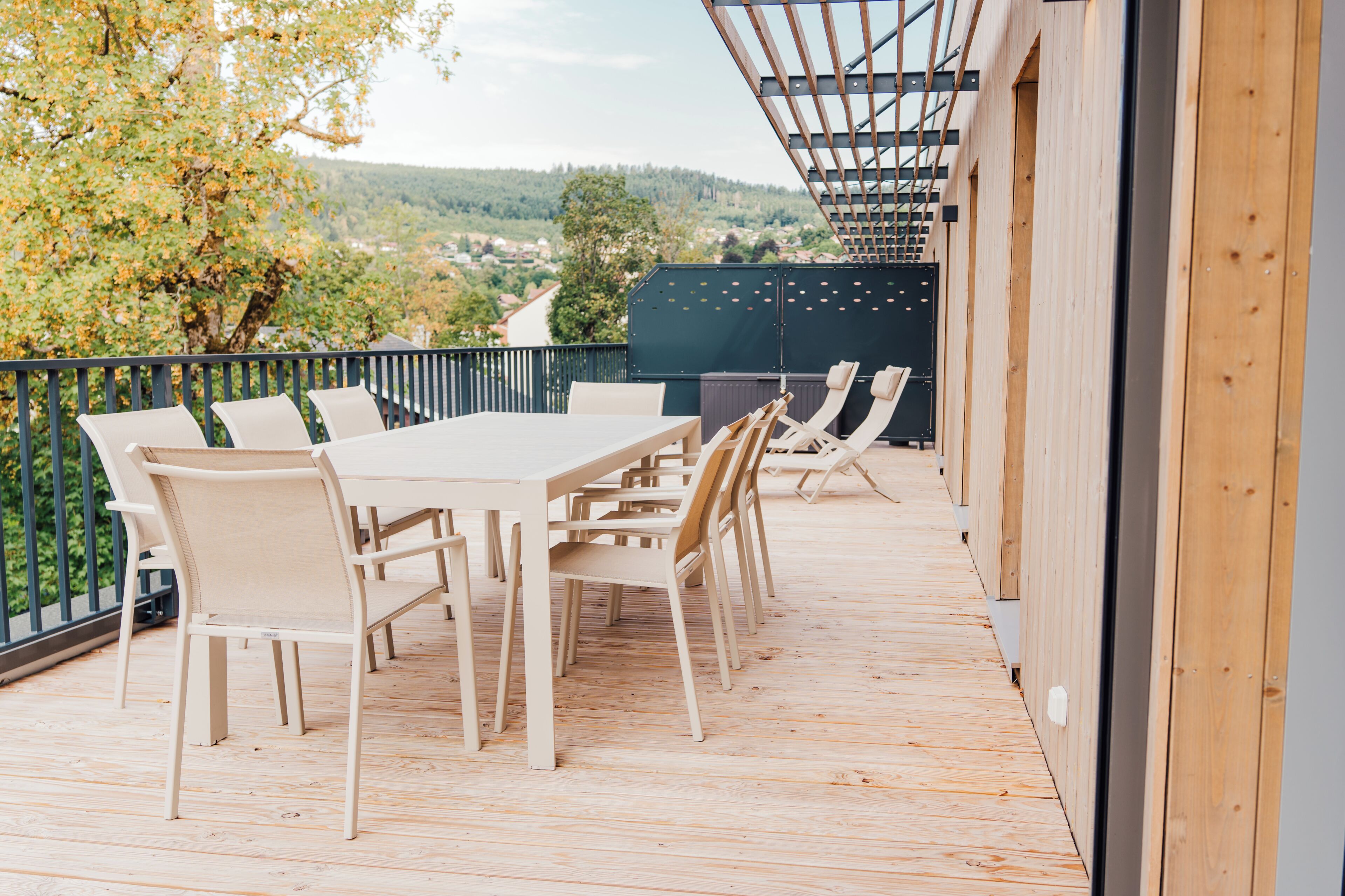 En udendørs terrasse med et bord og stole, med udsigt over et naturskønt landskab.