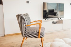 Ein modernes Wohnzimmer mit einem gemusterten Sessel, einem Flachbildfernseher und einer schlichten weißen Unterhaltungseinheit.