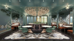 A modern interior with a central round table, green upholstered chairs, and a decorative ceiling light fixture.