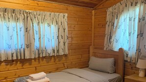 A cabin with two beds, wooden walls, and curtains with deer prints.