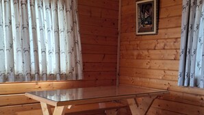 A wooden interior with a long table and benches, a framed picture on the wall, and patterned curtains.