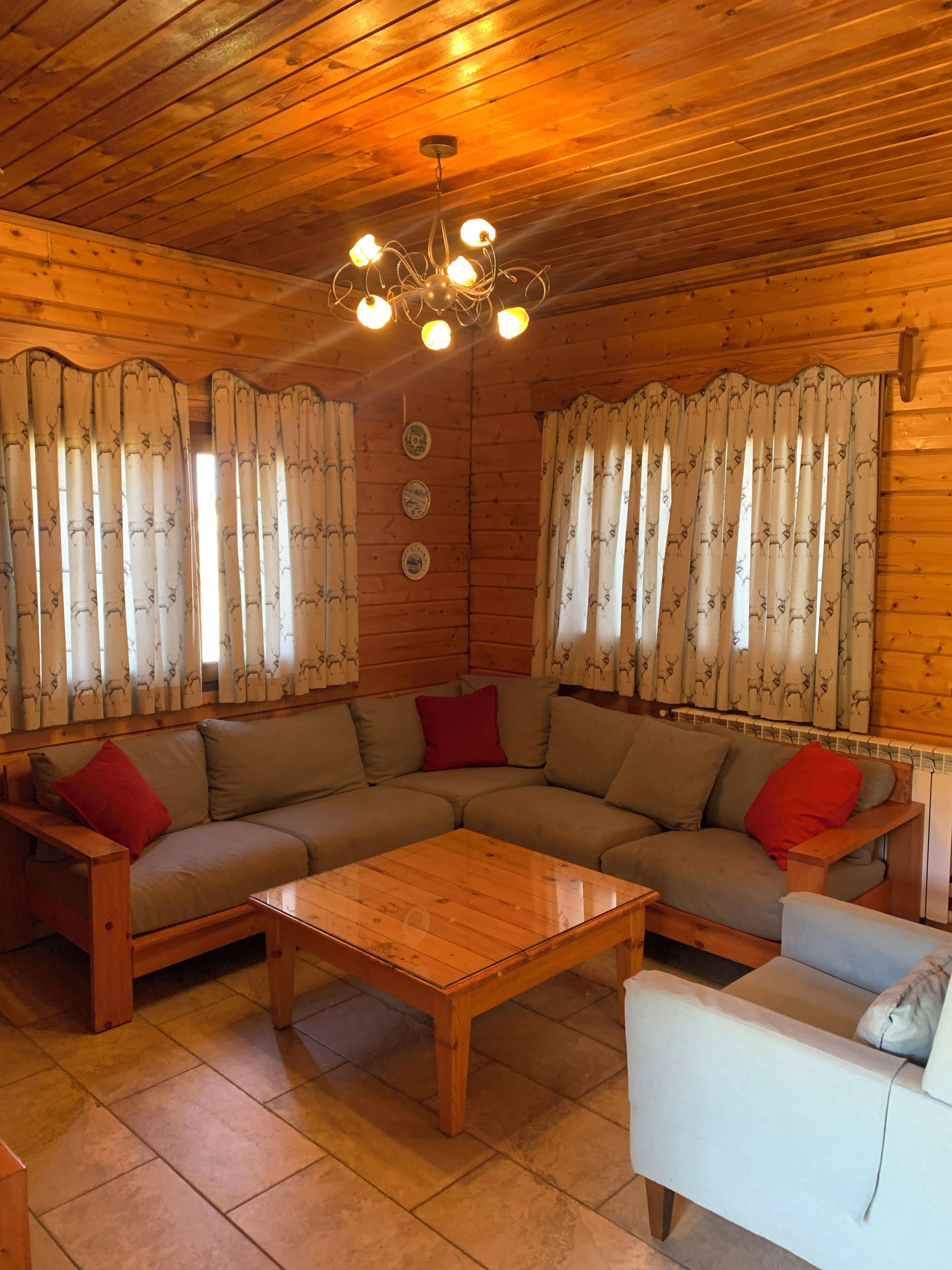 Interior acogedor de una cabaña con techo de madera, un sofá modular, una mesita y cortinas con estampados de animales.