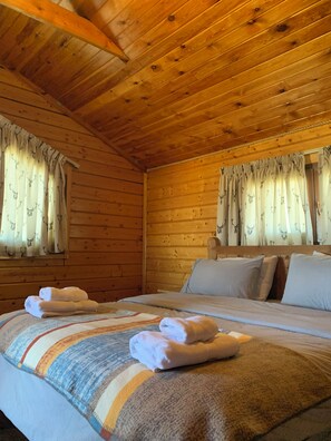 A wooden cabin room with a bed, pillows, and curtains with animal prints.