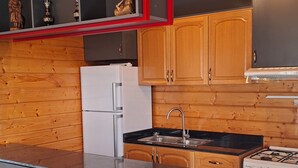 A modern kitchen with wooden cabinetry, a central island, stainless steel appliances, and a red-framed shelf with decorative items.