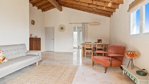 A spacious living area with a high wooden ceiling, a grey sofa, a red armchair, a dining table with chairs, and a floor lamp. - Holiday Home 'Paradise in Andalusia' with Mountain View, Wi-Fi and Air Conditioning (Tolox)