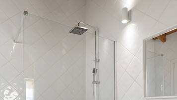 Un baño moderno con ducha de mampara de vidrio, un lavamanos blanco y un perchero para toallas.
