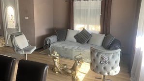 Uma sala de estar com um sofá, duas poltronas, uma mesa de centro de vidro e uma estátua dourada.
