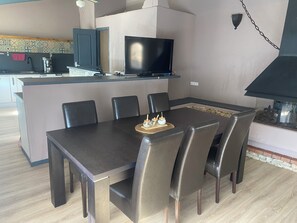 Ein Essbereich mit Tisch, Stühlen, einem Fernseher und einer Küche im Hintergrund.
