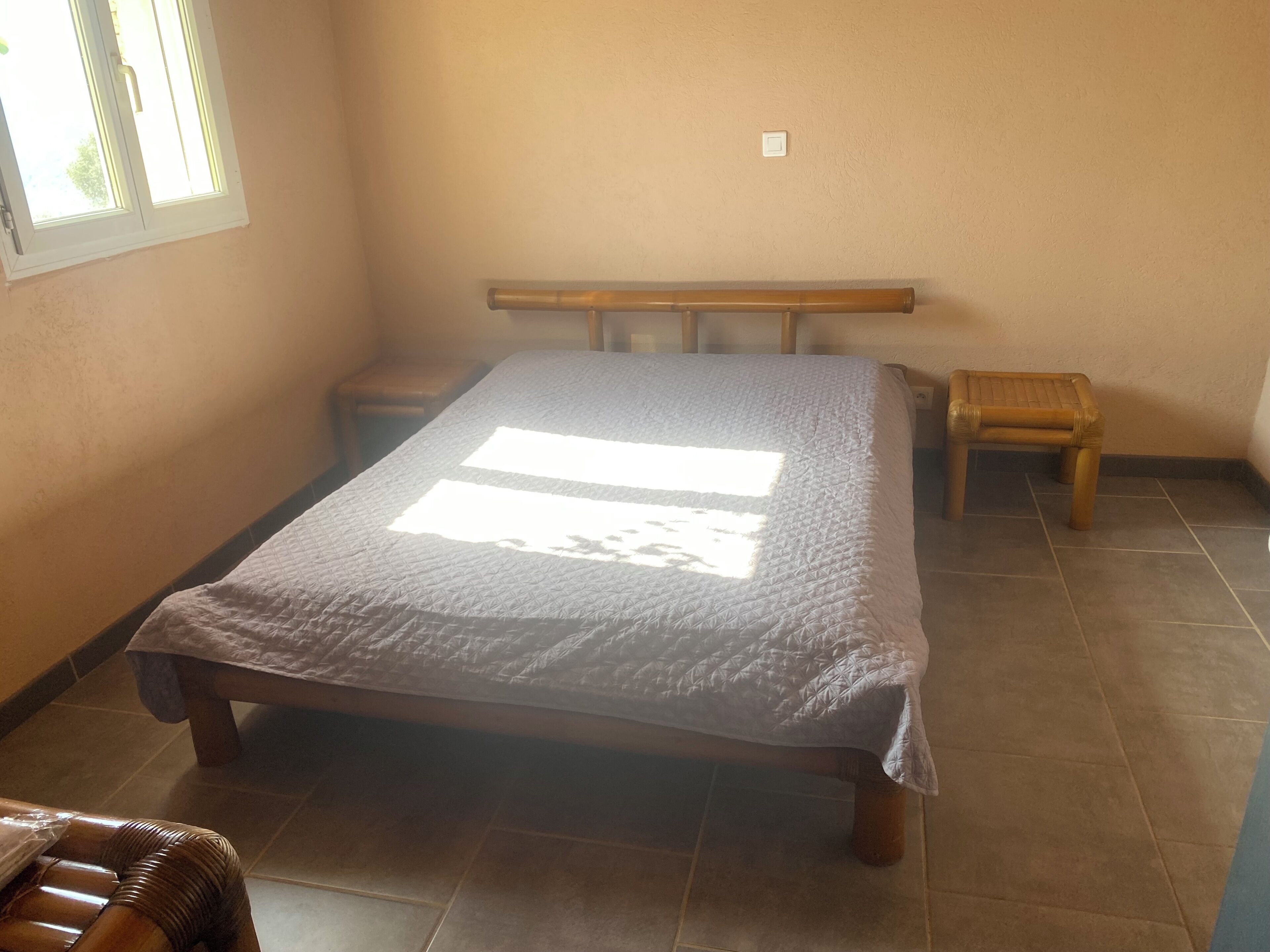 A bedroom with a bed, a bench, a small table, and a window.