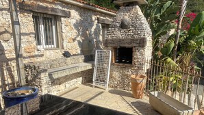 A stone building with a pool, a grill, and a fenced area with plants.