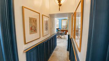 A hallway with framed artwork on the walls, a blue railing, and a dining area in the background.