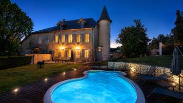 Una casa grande con piscina, un muro de piedra y una terraza de madera.