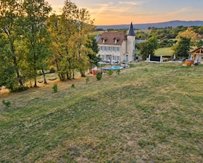 A large house with a swimming pool, surrounded by trees and a hilly landscape.