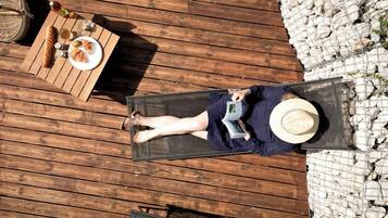 Una persona recostada sobre una cubierta de madera, con sombrero, leyendo un libro.