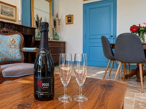Una botella de vino espumoso M 1931 Seyssel Brut, dos copas vacías, una puerta azul, una silla azul y una mesa de madera.