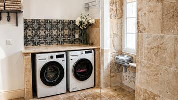 Een moderne badkamer met een douche, twee wasmachines en een betegelde vloer.