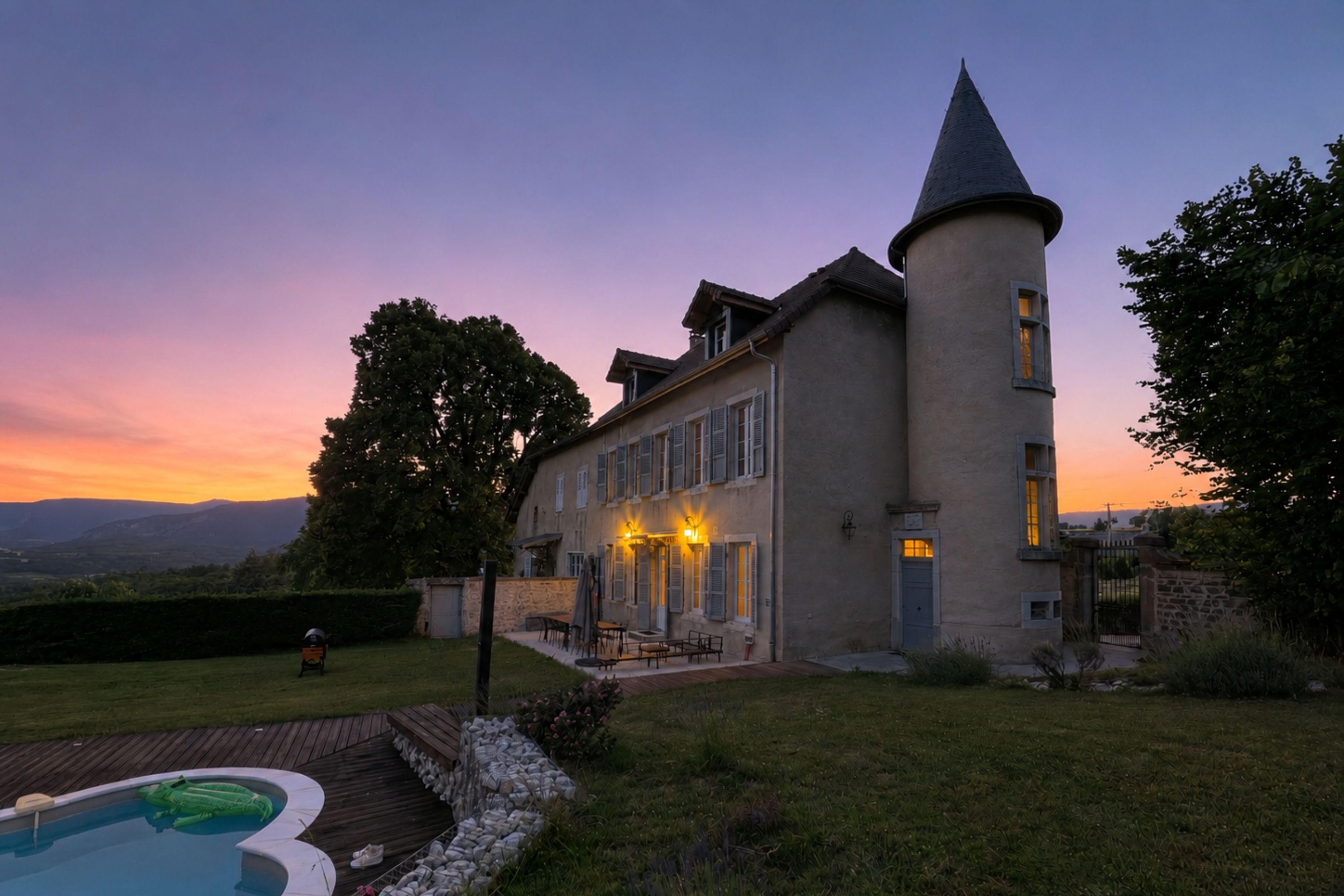 A large house with a tower, a swimming pool, and a well-maintained lawn.