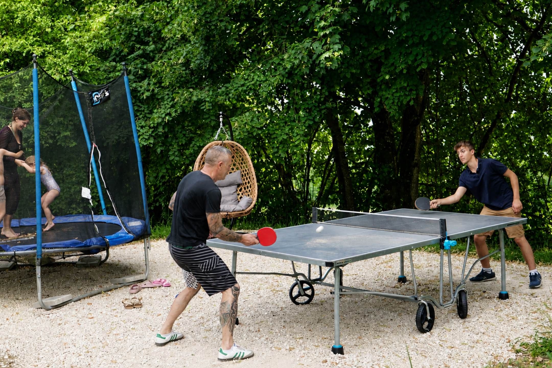 Ulkokäyttöön tarkoitettu pöytätennissetti, jossa on verkko ja joka on sijoitettu puiden ympäröimään paikkaan.